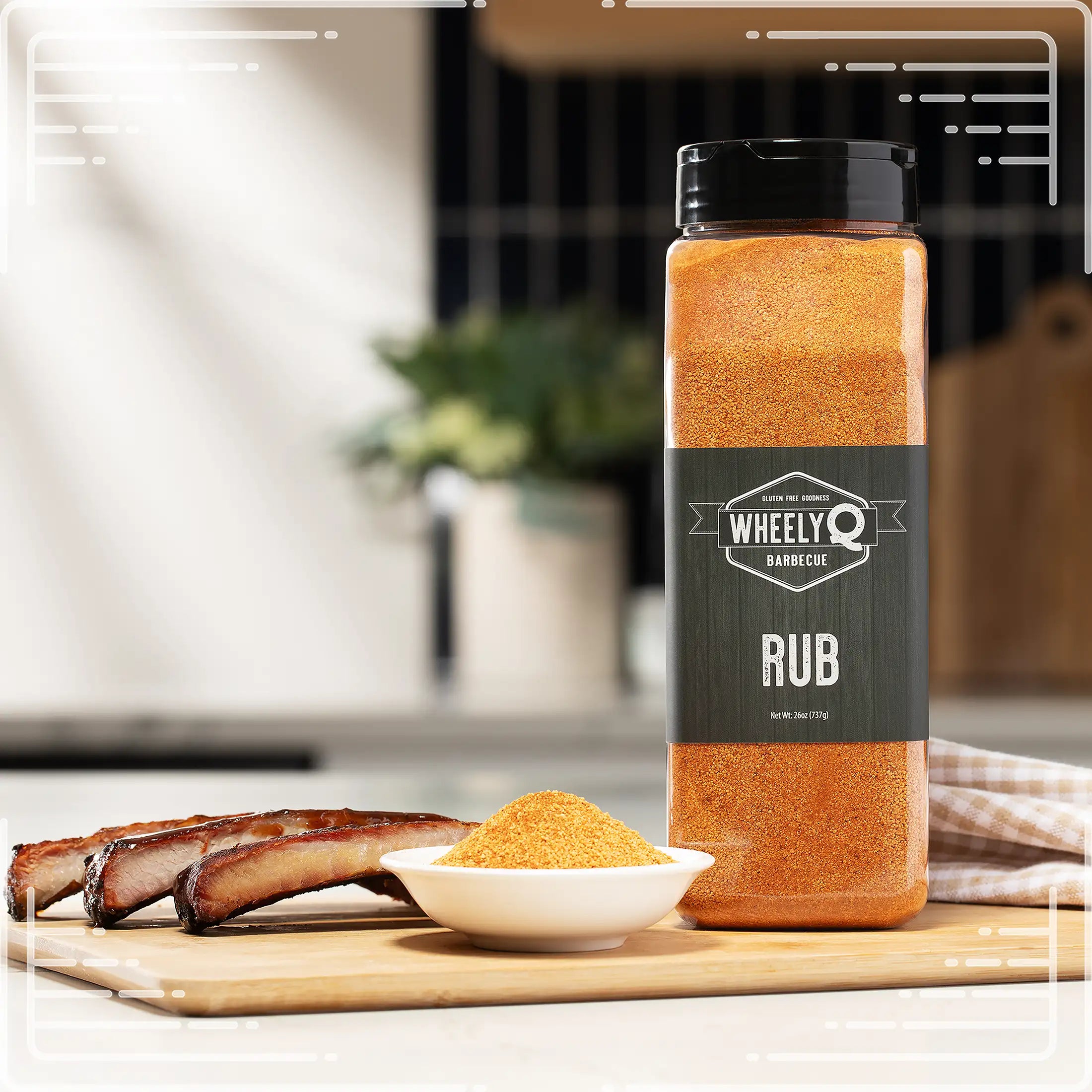 WheelyQ Barbecue All-Purpose Rub 26oz shaker bottle sitting on a cutting board in a kitchen.  On the cutting board is also a little white bowl full of the seasoning with 3 ribs on the left.