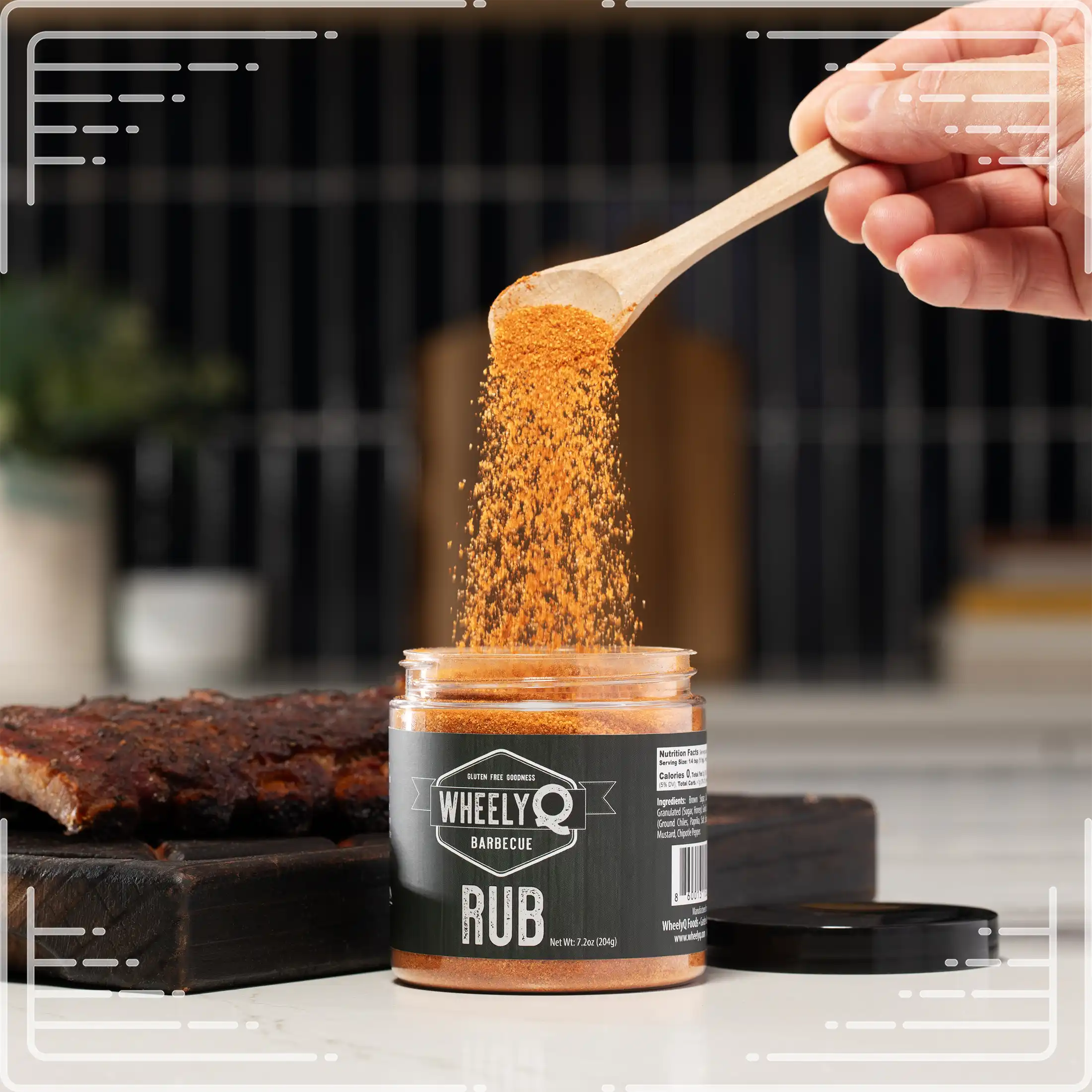 WheelyQ Barbecue All-Purpose Barbecue Rub being poured from a wooden spoon into a jar with a blurred kitchen background.