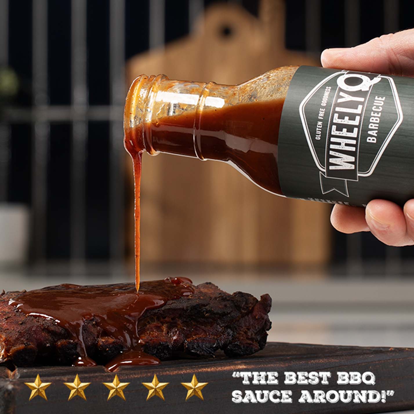 Bottle of WheelyQ Barbecue Original Recipe Barbecue Sauce being poured onto a piece of meat with a five-star rating and text 'The best BBQ sauce around!' in the foreground.