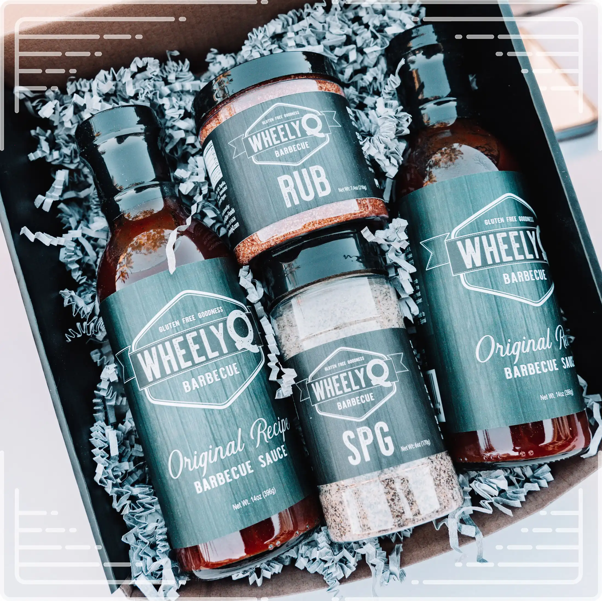 An image of a Barbecue Gift Box sold by WheelyQ Barbecue.  The gift set include 2 bottles of Barbecue Sauce, 1 bottle of SPG Seasoning and 1 jar of All-Purpose Rub or Ancho Espresso Seasoning.