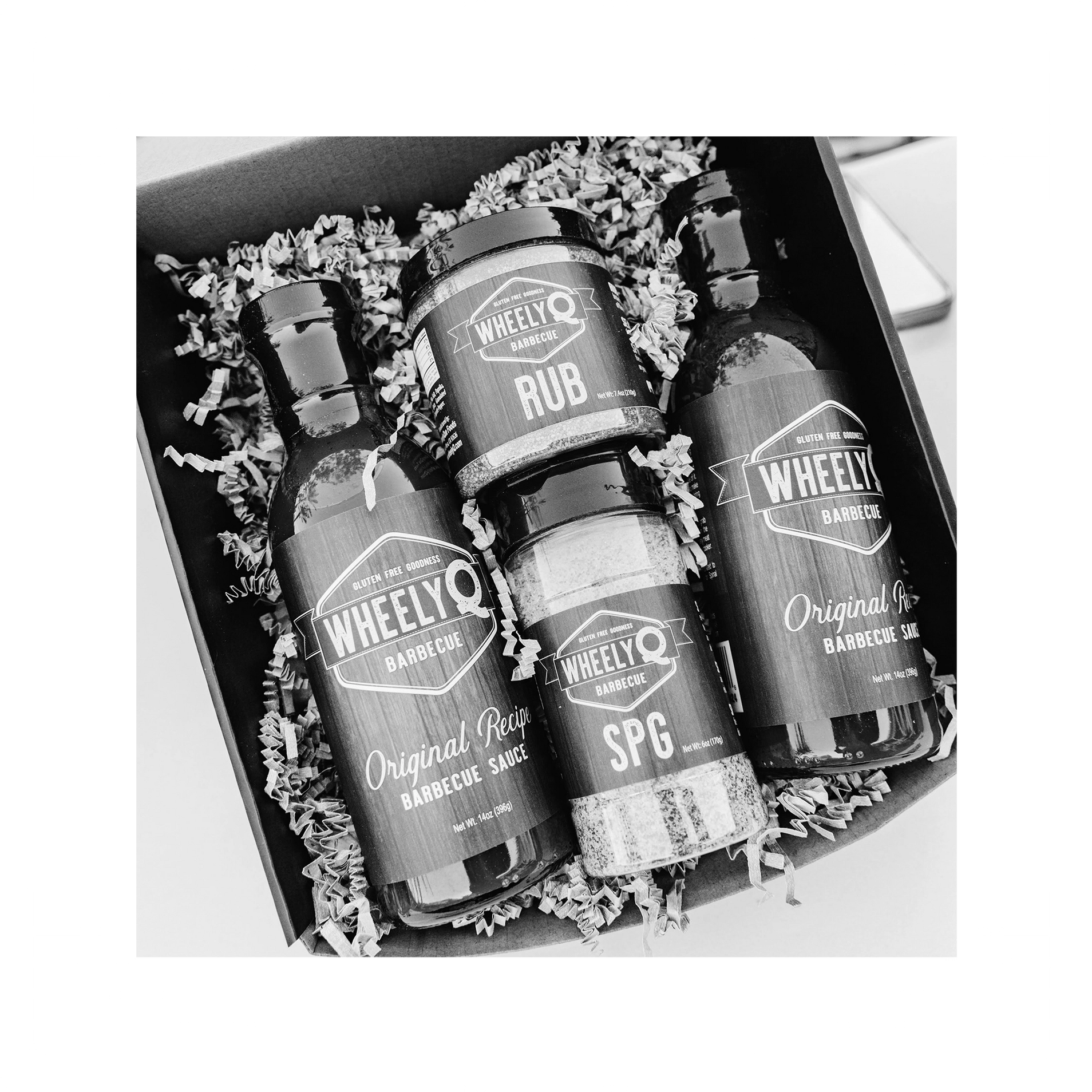 An image of a Barbecue Gift Box sold by WheelyQ Barbecue.  The gift set include 2 bottles of Barbecue Sauce, 1 bottle of SPG Seasoning and 1 jar of All-Purpose Rub or Ancho Espresso Seasoning.