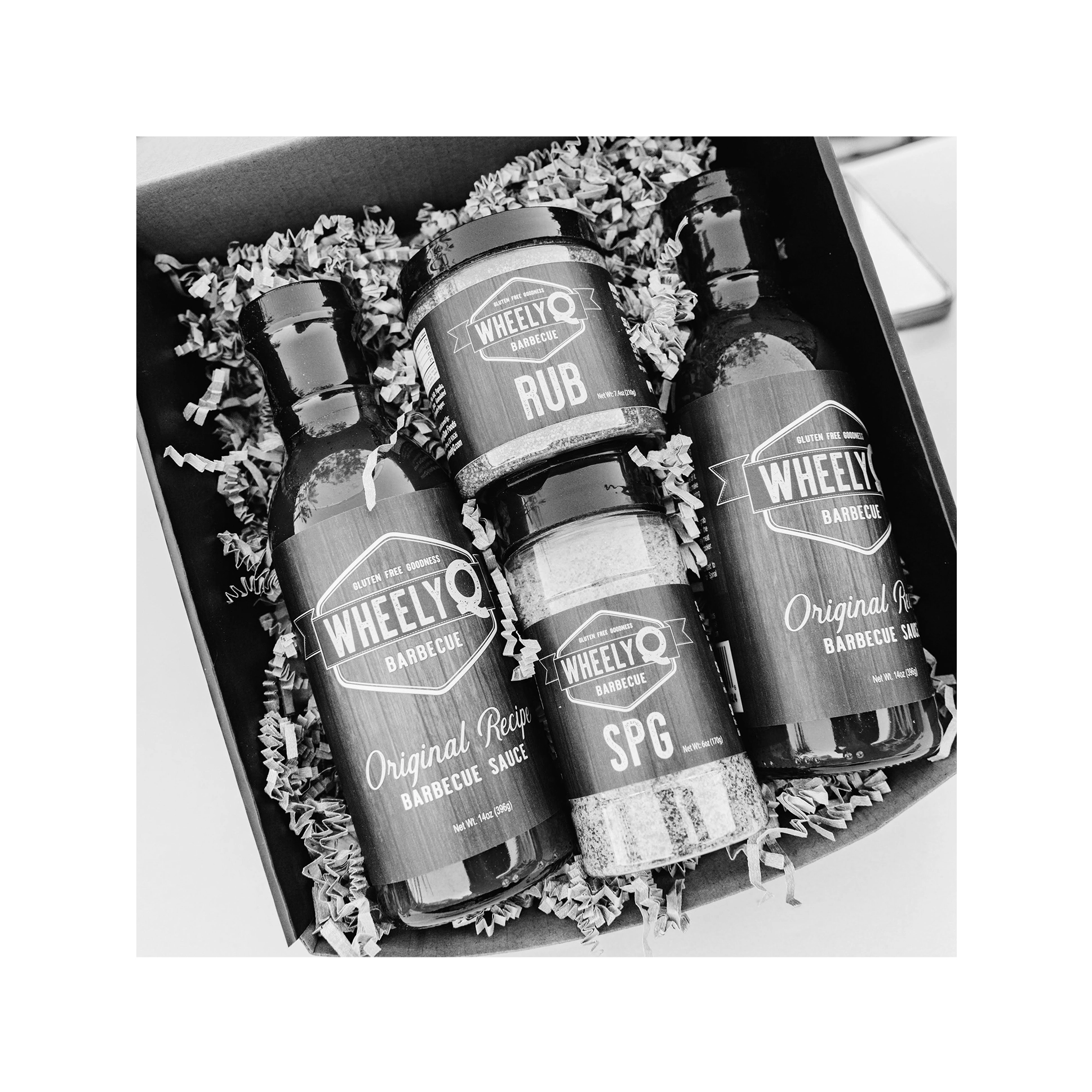 An image of a Barbecue Gift Box sold by WheelyQ Barbecue.  The gift set include 2 bottles of Barbecue Sauce, 1 bottle of SPG Seasoning and 1 jar of All-Purpose Rub or Ancho Espresso Seasoning.