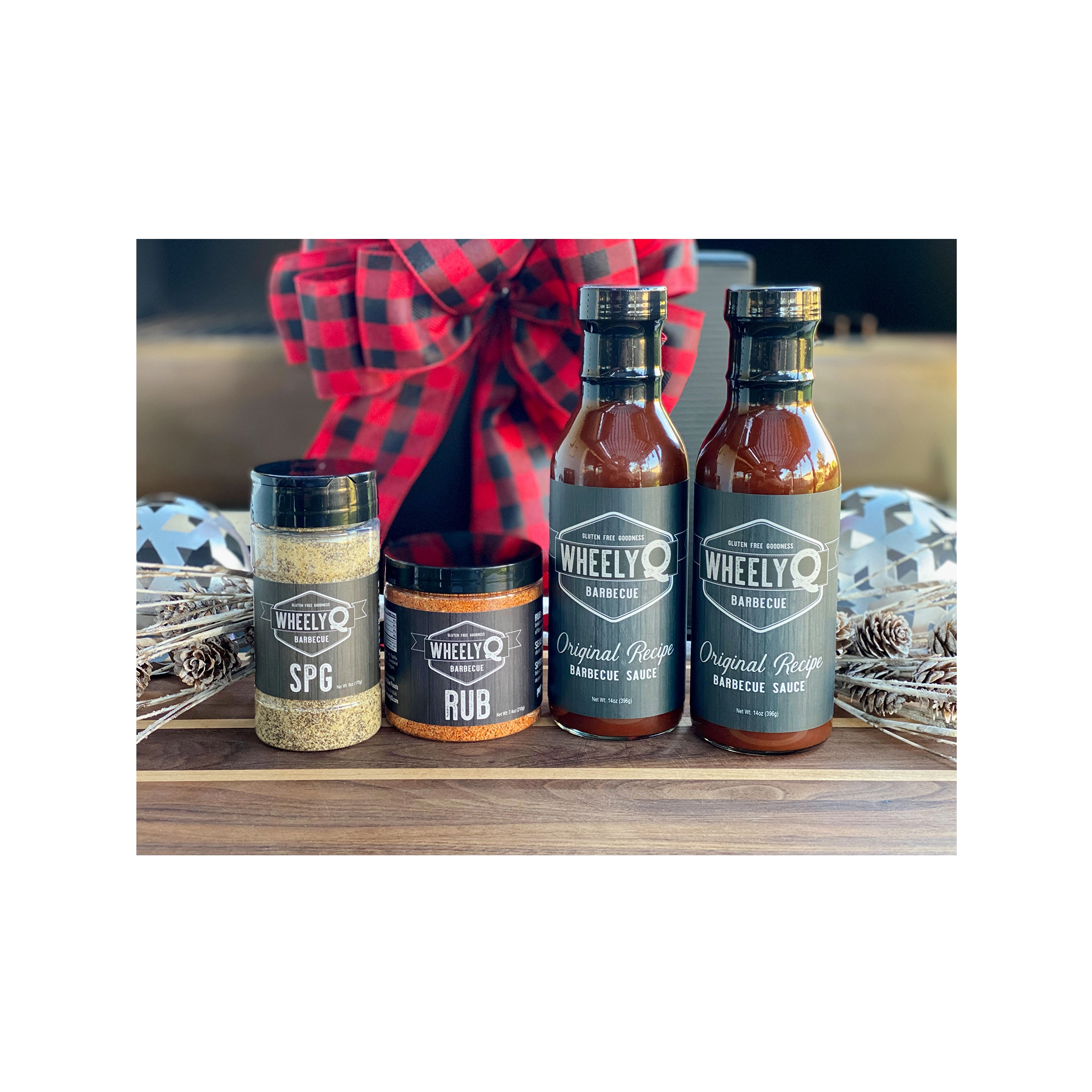 An image of a Barbecue Gift Box sold by WheelyQ Barbecue.  The gift set include 2 bottles of Barbecue Sauce, 1 bottle of SPG Seasoning and 1 jar of All-Purpose Rub or Ancho Espresso Seasoning.