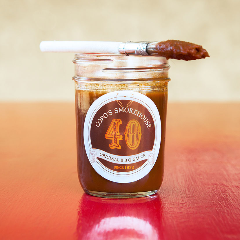 Image of a mason jar of barbecue sauce with a brush laying on top that was dipped in sauce.