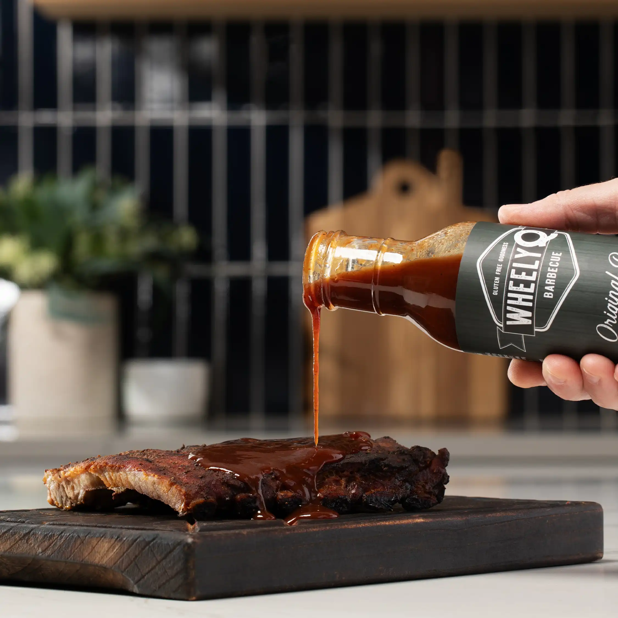 Hand pouring a bottle of WheelyQ Barbecue Original Recipe Barbecue Sauce onto ribs.
