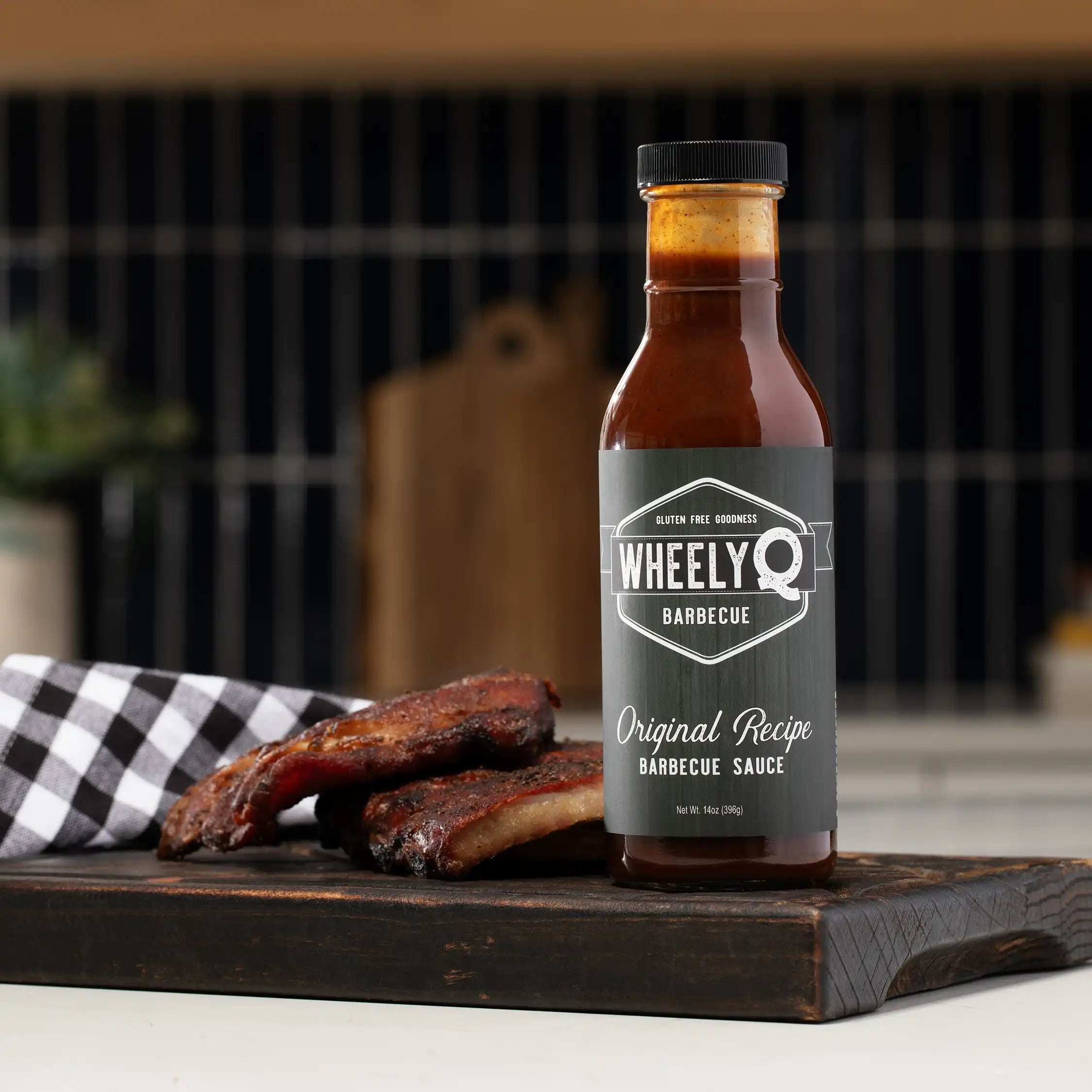 WheelyQ Barbecue Original Recipe Barbecue Sauce on a wooden cutting board with ribs, against a blurred kitchen background.