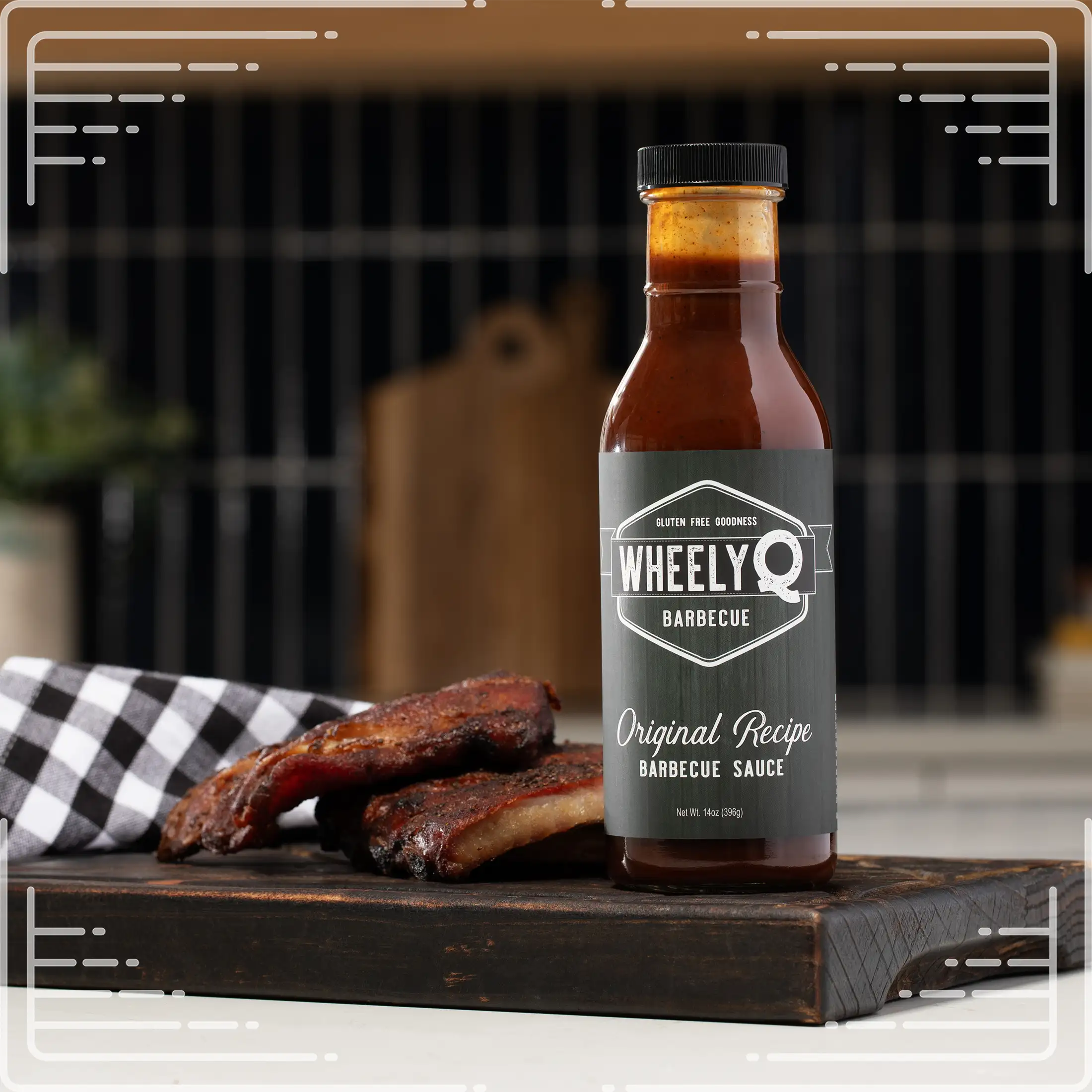Bottle of WheelyQ Barbecue Original Recipe Barbecue Sauce on a wooden cutting board with ribs, against a blurred kitchen background.